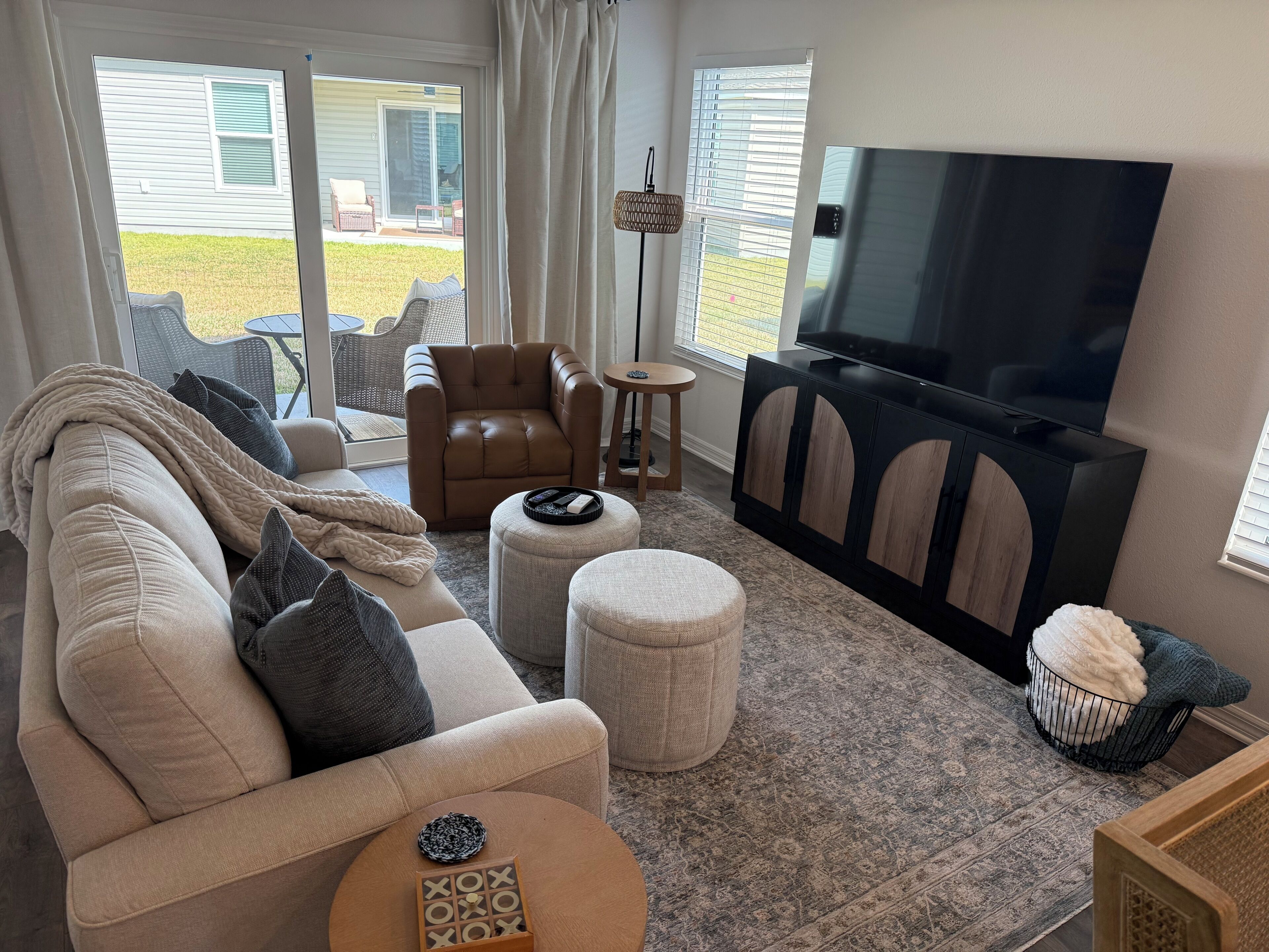 Un salon comprenant un canapé, un pouf, un meuble pour la télévision et donnant sur l’extérieur.