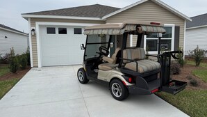 A golf cart parked in front of a house with a garage, a driveway, and a small garden area. - The Villages-Adorable Patio Villa with golf car located close to entertainment. (Sumterville)