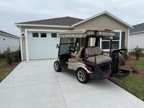 Ein Golfmobil steht vor einem Haus mit Garage, Auffahrt und einem kleinen Garten.