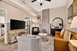 A modern living room with a flat-screen TV, a grey armchair, a brown sofa, and a small round coffee table. - Row Home in Victorian District w/ Parking + Pet-friendly by Lucky Savannah (Savannah)