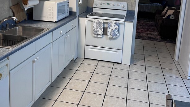 A kitchen with white cabinets, a microwave, a stove, and a ceiling fan.