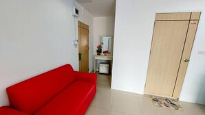 A room with a red sofa, a wooden wardrobe, a small table with a mirror, and a tiled floor. - Orca Guesthouse (Pattaya)