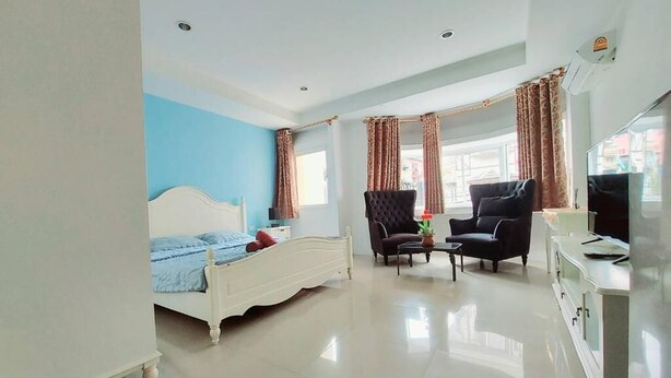 A bedroom with a bed, a chair, a table, and a TV. - Orca Guesthouse (Pattaya)