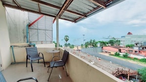 A balcony with chairs and a small table, overlooking a cityscape with buildings and a road. - Orca Guesthouse (Pattaya)