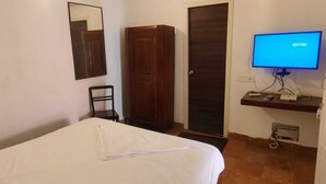 Ein Hotelzimmer mit einem Bett, einem Kleiderschrank, einem Fernseher und einem Schreibtisch mit Computer und weiteren Gegenständen.
