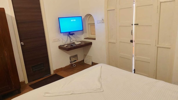 Ein Hotelzimmer mit Bett, Wandfernseher, kleinem Schreibtisch mit Computer und einer Tür.
