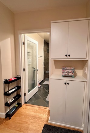 A hallway with a white wardrobe, a glass door leading to a bathroom, and a black shelf unit. - Bright and spacious guest suite (Burbank)
