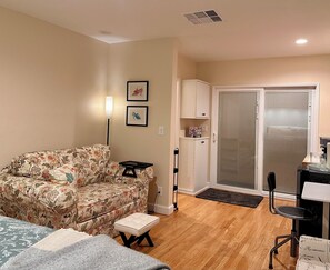 A room with a floral sofa, a small table, a chair, a cabinet, and a sliding glass door. - Bright and spacious guest suite (Burbank)
