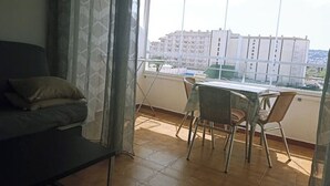 Ein Balkon mit Esstisch und Stühlen, einer Couch und Blick auf ein gegenüberliegendes Gebäude.