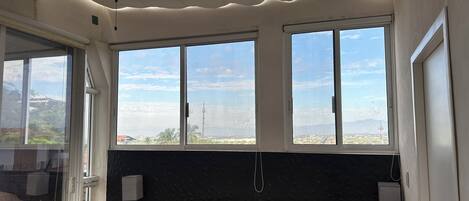 Un dormitorio con cama, ventilador de techo, ventana grande con vistas y mesita de noche.