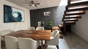 A dining area with a wooden table and white chairs, a ceiling fan, a dark textured wall, and a staircase with wooden steps. - Mango house (Puerto Vallarta)