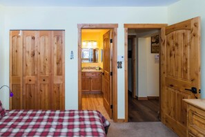 A bedroom with a plaid bedspread, wooden wardrobe, and a small kitchenette with a mirror and lights. - Beaver Village Unit #0233 Renovated 2 bed vaulted ceilings, hardwood floor (Winter Park)