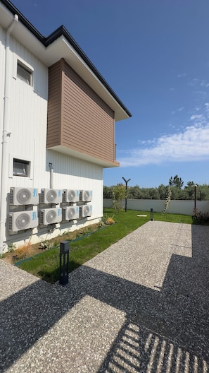 Een modern gebouw met een witte gevel, een bruin gedeelte bovenin en meerdere airconditioning units.