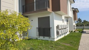 A two-story residential building with a balcony, air conditioning units, and a grassy yard. - Nest Park Side | Evrenseki
 Modern & Lüks Daireler
 Havuzlu Site (Antalya)