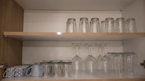 A kitchen shelf with glass jars and wine glasses.