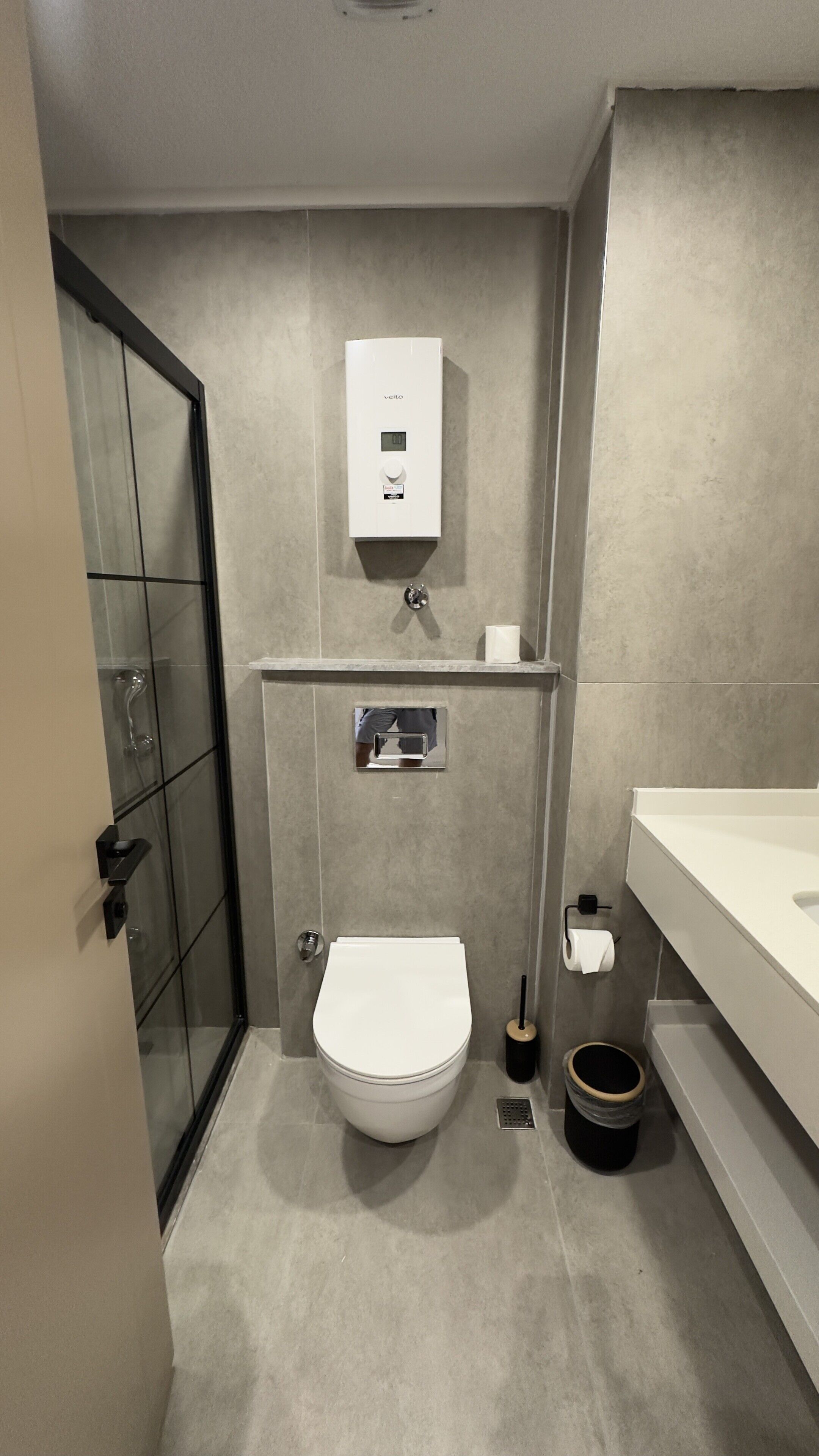 Un baño moderno con inodoro, cabina de ducha, calefacción integrada y lavabo con espejo.