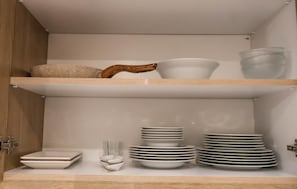 A kitchen cabinet with shelves holding various dishes and a wooden spoon.