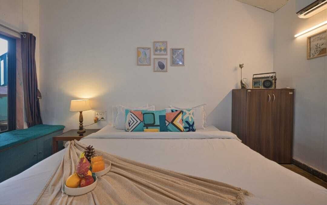 Una habitación de hotel con una cama, una mesita de noche con lámpara, una radio y una cesta de frutas sobre la cama.