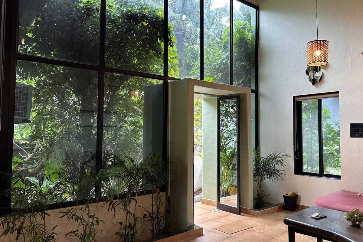 Una habitación con ventanas amplias, un colgador de macramé en la pared y un banco de madera.
