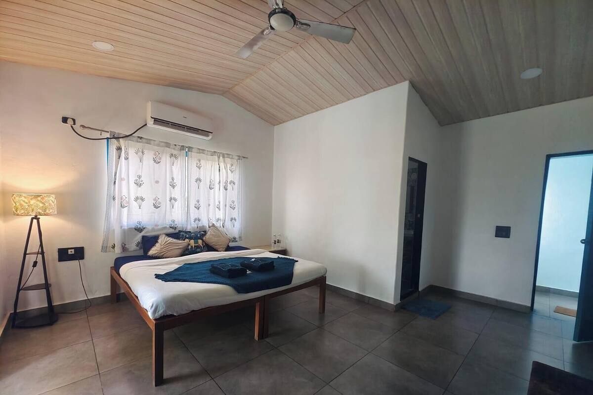 Un dormitorio con cama, mesita de noche, lámpara, equipo de aire acondicionado y ventilador de techo.