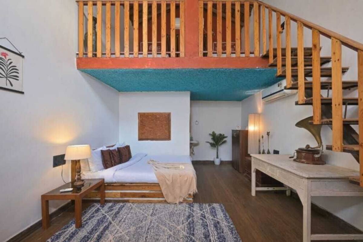Un dormitorio con cama, mesita de noche, lámpara y una pequeña mesa con un tocadiscos.