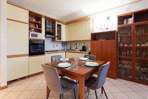 A compact kitchen with a dining table set for four, equipped with a microwave, oven, and various kitchen utensils.