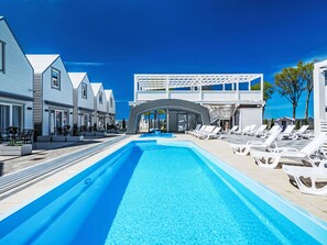 Piscina com espreguiçadeiras e área coberta, rodeada por edifícios modernos.
