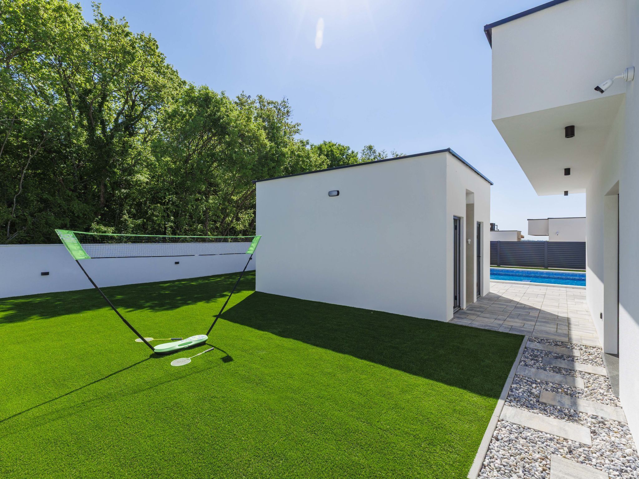 A modern outdoor area with artificial grass, a badminton net, and a swimming pool.