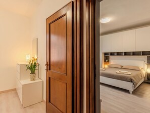 A bedroom with a bed, bedside table, lamp, and a wooden door. - La Finestra su Bellagio by Interhome (Varenna)