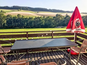 Una terraza de madera con una mesa, sillas y una sombrilla, con vistas a un campo de golf.