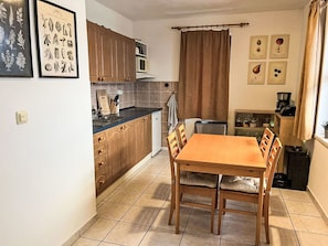 Una cocina compacta con armarios de madera, una mesa de comedor y sillas. Hay impresiones enmarcadas de motivos botánicos en la pared.