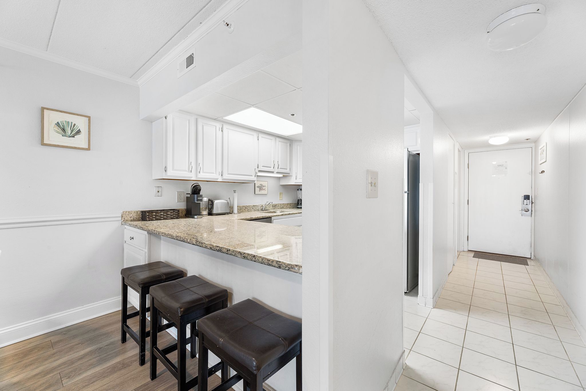 A modern kitchen with white cabinets, a granite countertop, and a built-in stove. There are three dark brown bar stools.
