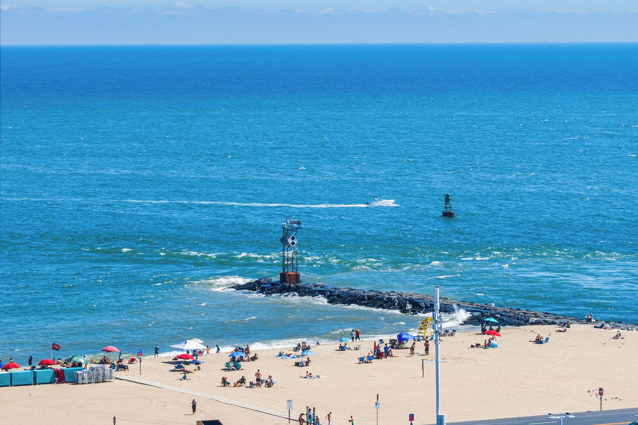 A beach with a rocky breakwater, umbrellas, and people sunbathing.
