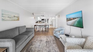 Ein modernes Wohnzimmer mit einem grauen Sofa, einem gemusterten Sessel und einem an der Wand befestigten Flachbildfernseher.
