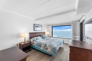 A hotel room with a bed, nightstands, a desk, a window with a view of the ocean, and a framed picture on the wall. - Marigot Beach 811 (Ocean City)