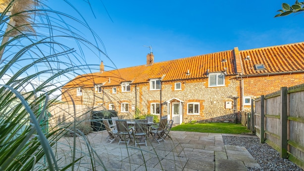 A two-story brick house with a tiled roof, a patio with a table and chairs, and a wooden fence. - 2 Ruscon Cottage,  Brancaster Staithe, Norfolk (Brancaster Staithe)