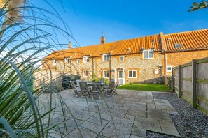 A two-story brick house with a tiled roof, a patio with a table and chairs, and a wooden fence. - 2 Ruscon Cottage,  Brancaster Staithe, Norfolk (Brancaster Staithe)