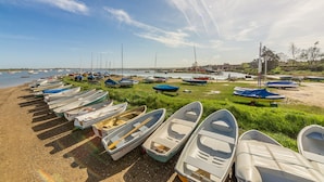 A row of small boats lined up on a sandy beach with a grassy area in the middle, and a calm body of water in the background. - 2 Ruscon Cottage,  Brancaster Staithe, Norfolk (Brancaster Staithe)