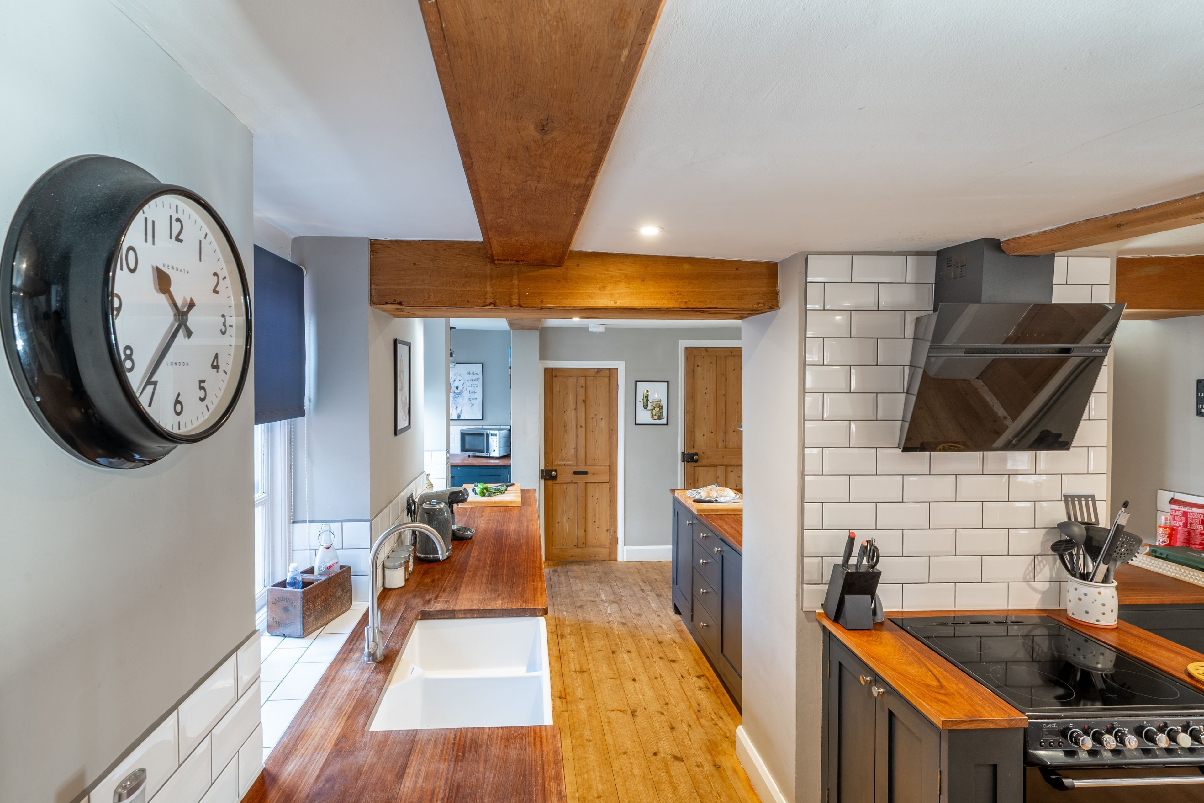 A modern kitchen with a wooden ceiling, a large wall clock, and a black stove.