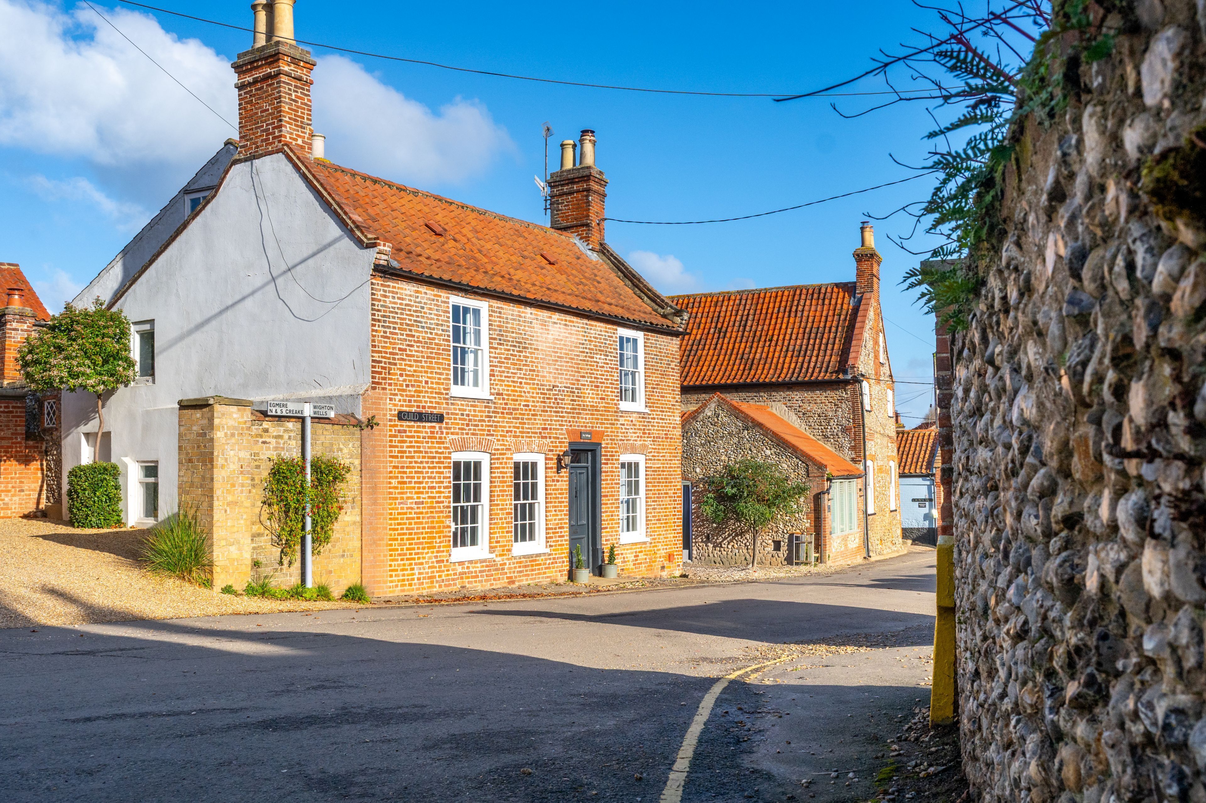 A traditional brick house with a tiled roof, a visible chimney, and a paved street in front.