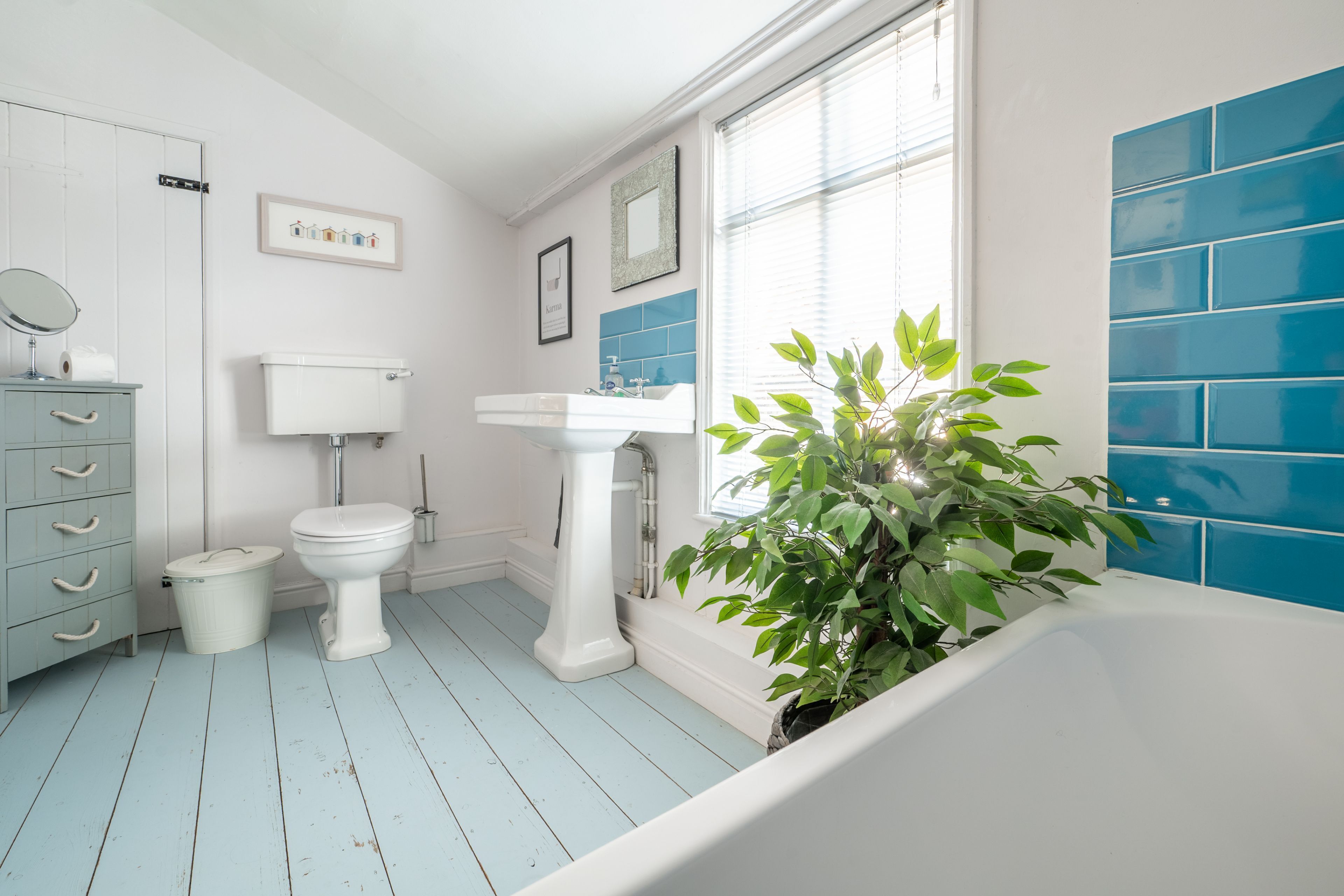 A bathroom with a white toilet, a white sink, a blue tiled wall, a white bathtub, and a green plant.