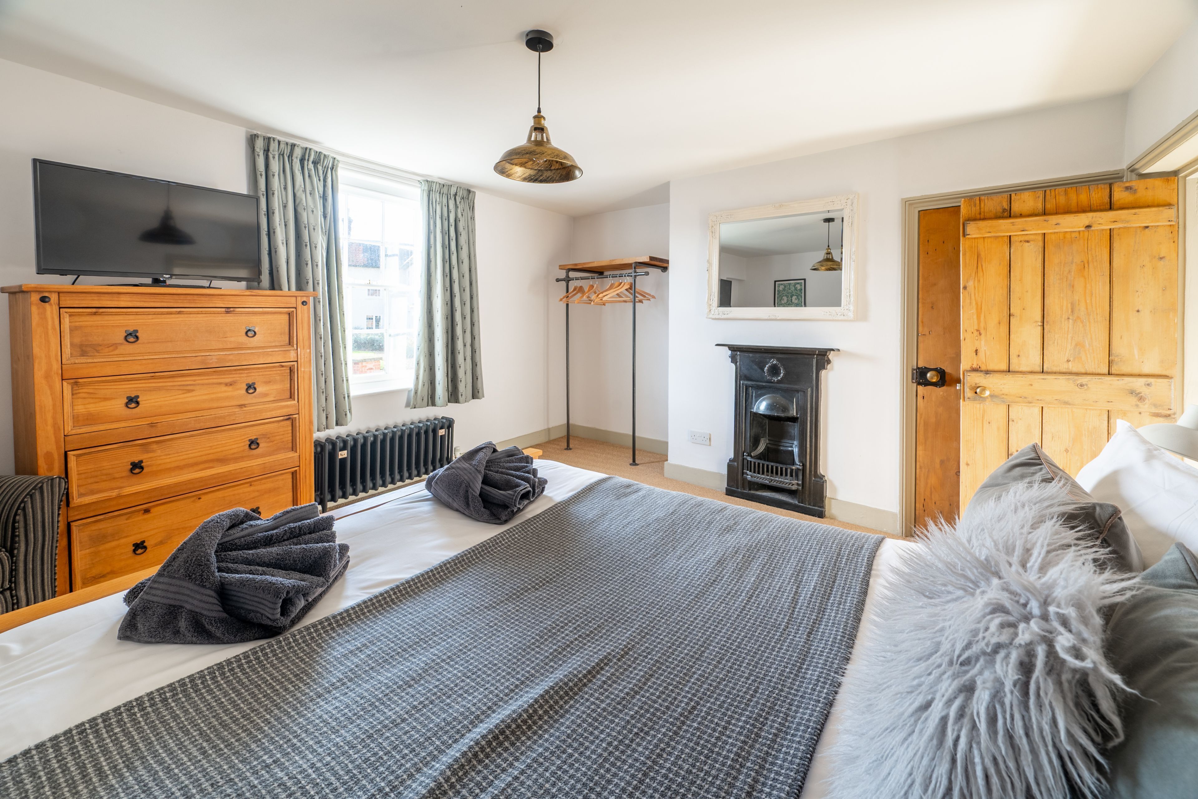 A bedroom with a bed, a wooden dresser, a television, a radiator, a mirror, and a wardrobe.