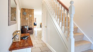 Un pasillo con pared de madera, un sofá de cuero marrón, una puerta blanca y una escalera con balaustres blancos.