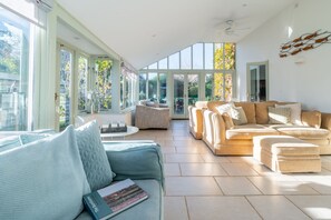 A spacious living room with a large window, a beige sofa, a blue sofa, and a coffee table. - Hornbeam, Burnham Market, Norfolk (Burnham Market)
