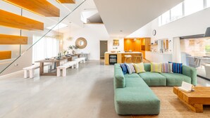 Un soggiorno moderno con un divano modulare verde, travi in legno, un'area pranzo e una cucina.