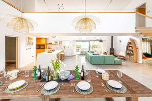 Ein stilvoller Essbereich mit einem Holztisch, gedeckt für eine Mahlzeit, einer Küche im Hintergrund und einem grünen Sofa im Wohnbereich.