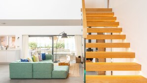 Un soggiorno moderno con un divano verde, una scala in legno e una cucina sullo sfondo.