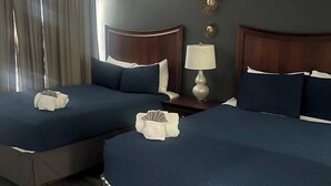Hotellihuone, jossa on kaksi sänkyä, kattotuuletin, yöpöytä lampun kanssa ja koristeellinen seinäelementti.