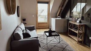Uma sala de estar moderna com um sofá, uma mesa de centro e uma estante de madeira. Há uma janela grande e uma porta que dá para o exterior.