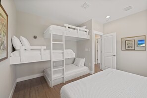 A bunk bed room with a door leading to another room, a framed picture on the wall, and a ceiling vent. - Steele Away by Liquid Life (Gulf Shores)